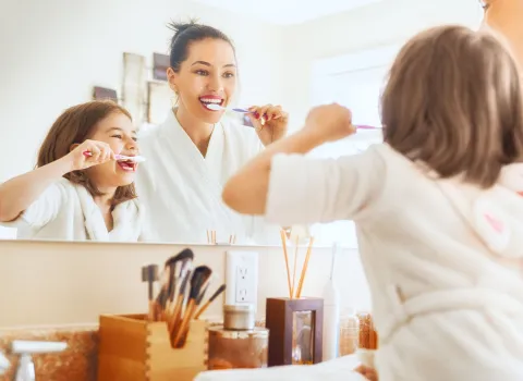 Frau und Kind putzen Zähne vor hellen Badezimmer-Spiegel.