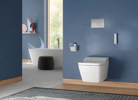 Großes Badezimmer mit blauen Wänden, einem wandhängenden TOTO-SW-WC und einer freistehenden Badewanne im Hintergrund.