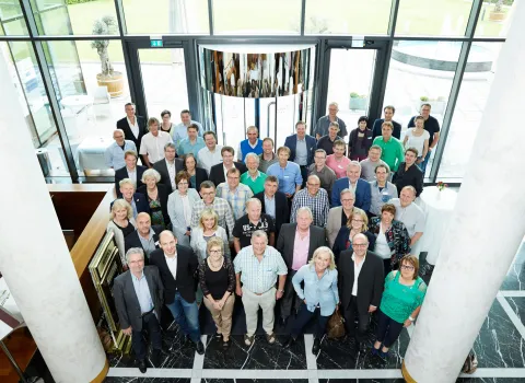 Eine große Gruppe von Menschen posiert in einem modernen Gebäude mit einer Glasfassade für ein Gruppenfoto.