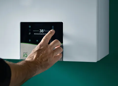 Eine Hand stellt die Warmwassertemperatur auf 38 Grad am digitalen Display eines Vaillant-Gasbrennwertgeräts ein.