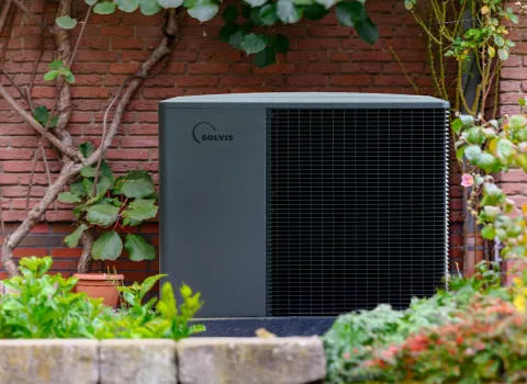 Wärmepumpe SolvisLea Pro von Solvis vor einer Ziegelwand in einem Garten.