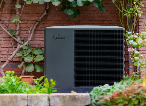 Wärmepumpe SolvisLea Pro von Solvis vor einer Ziegelwand in einem Garten.
