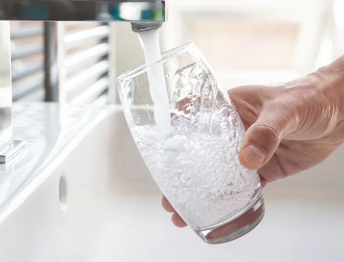Ein Wasserglas wird von einer Hand unter den Hahn gehalten, während frisches Trinkwasser mit sichtbaren Blasen eingefüllt wird.